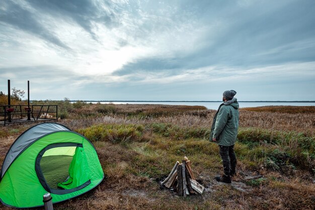 A bearded man near a camping tent in green  nature and the lake.  travel, tourism, camping.