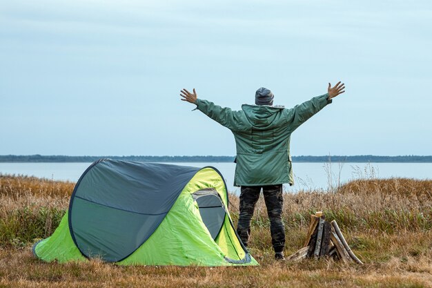 A bearded man near a camping tent in green  nature and the lake.  travel, tourism, camping.