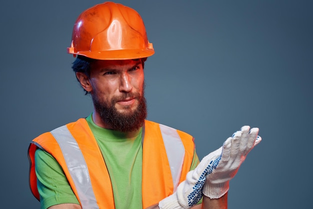 Bearded man in orange hard hat gloves professional cropped view blue background High quality photo