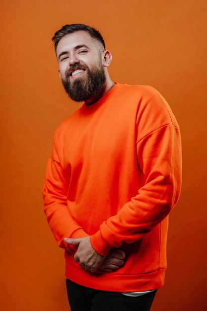 Photo a bearded man in an orange sweater stands with his arms crossed in front of him