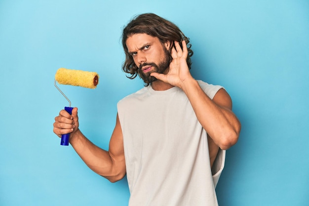 Bearded man painting with a yellow roller trying to listening a gossip