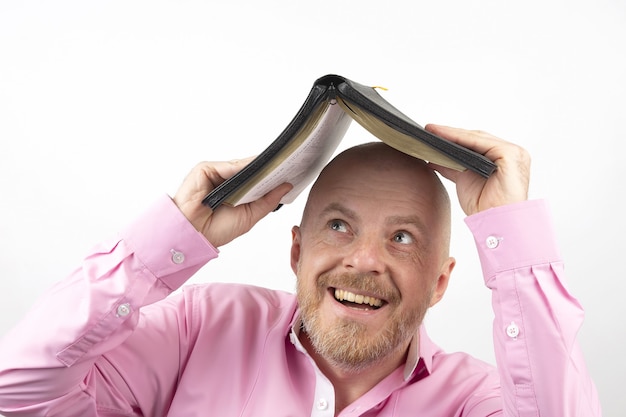 Bearded man in a pink shirt hides his head under an open Bible