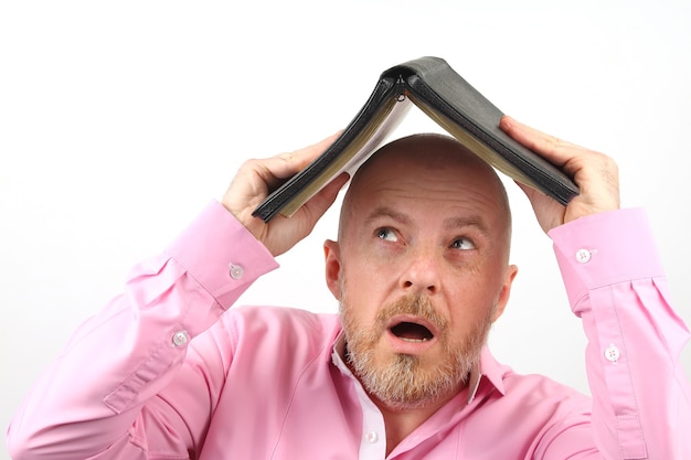 ピンクのシャツを着たひげを生やした男は、開いた聖書の下に頭を隠します