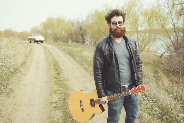 Bearded man playing guitar, near retro car