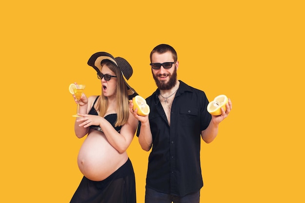 A bearded man and a pregnant girl in a bathing suit on a yellow background Refreshing fruits and drinks