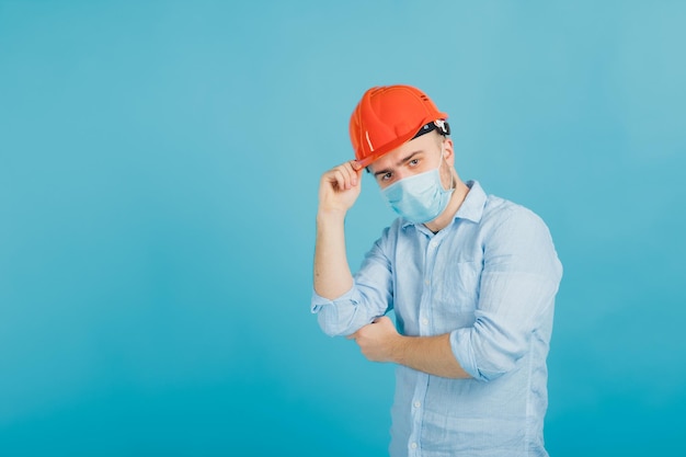 bearded man in a protective orange helmet and mask on a blue background