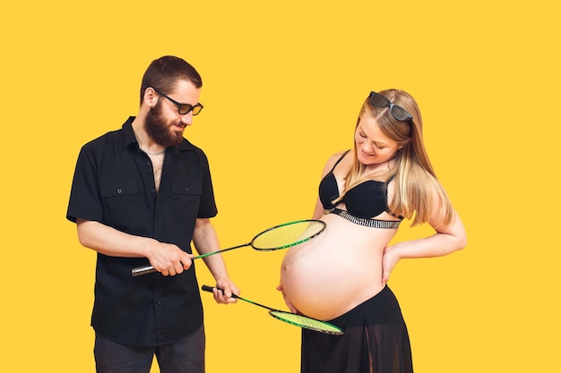 The bearded man puts tennis rackets to the stomach of his pregnant wife as if to the ball