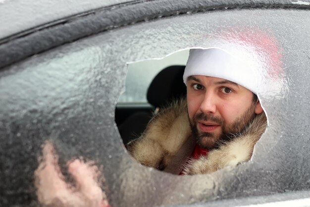 Bearded man in a red cap of Santa Claus in a car with broken glass