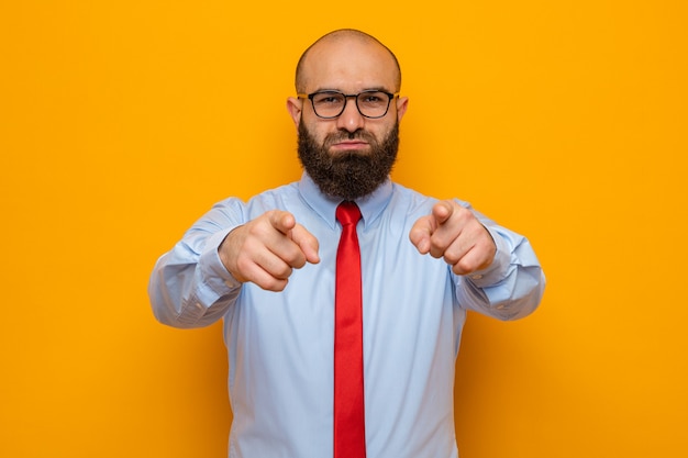 Bearded man in red tie and shirt wearing glasses pointing with index fingers at front, looking confident