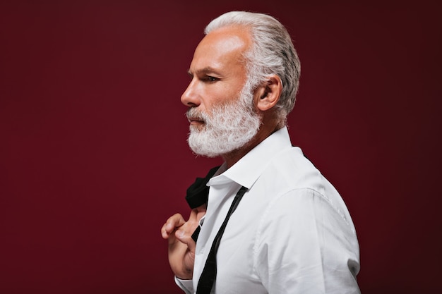 Bearded man in shirt poses on burgundy wall