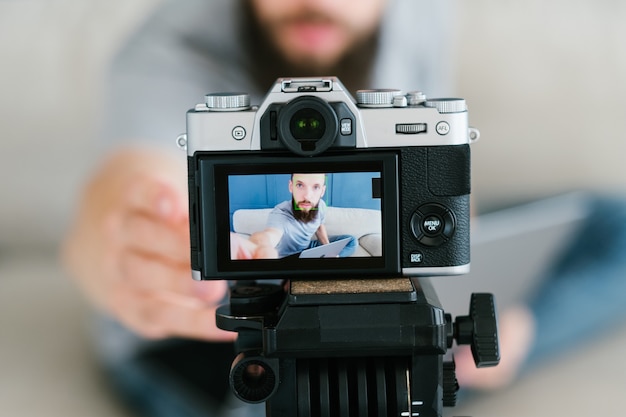 bearded man shooting video of himself using camera on tripod and creating content for social media.