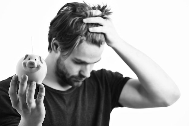 Bearded man short beard Caucasian sexy young macho with stylish hair and moustache on serious face holding pink piggy pig bank in blue shirt isolated on white studio background selective focus