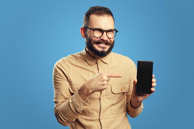 青い背景の上に分離された空白の画面の携帯電話を示すひげを生やした男