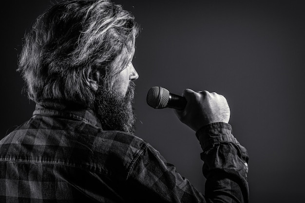 Bearded man singing with microphone. male singing with a\
microphones. man with a beard holding a microphone and singing.\
bearded man in karaoke sings a song into a microphone. male attends\
karaoke.