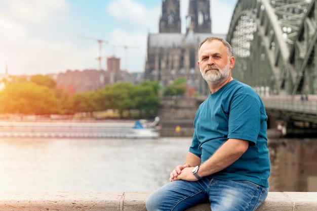 Bearded man sitting on embankment of Rhine on background of Cologne Cathedral