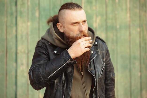 Bearded man smoking weed near wooden fence outdoors