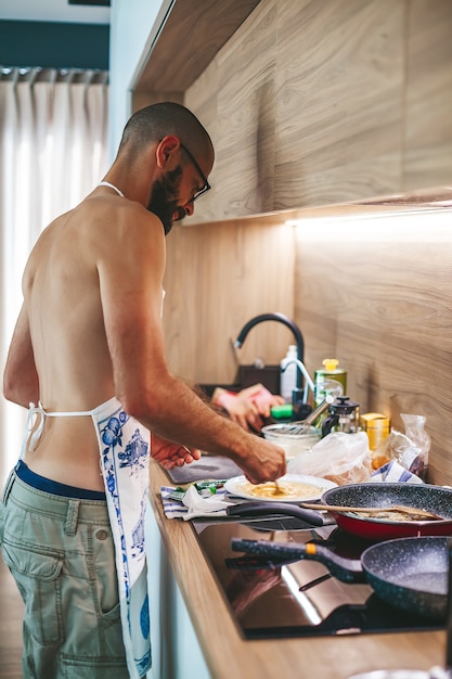 Bearded man standing in the kitchen cooking on the hob, using a spatula and frying pan