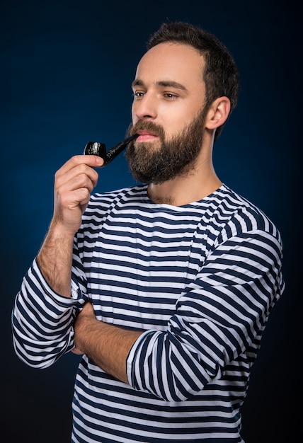 Bearded man in striped clothing is smoking a pipe.