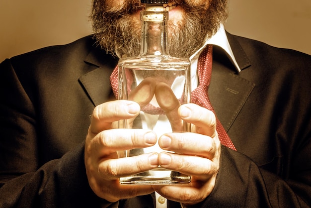 Bearded man in suit holding a bottle with alcohol in front of him Toned