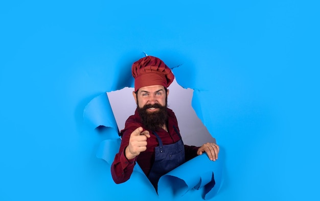 Bearded man through paper chef professional chef points forward bearded cook in kitchen chief man in