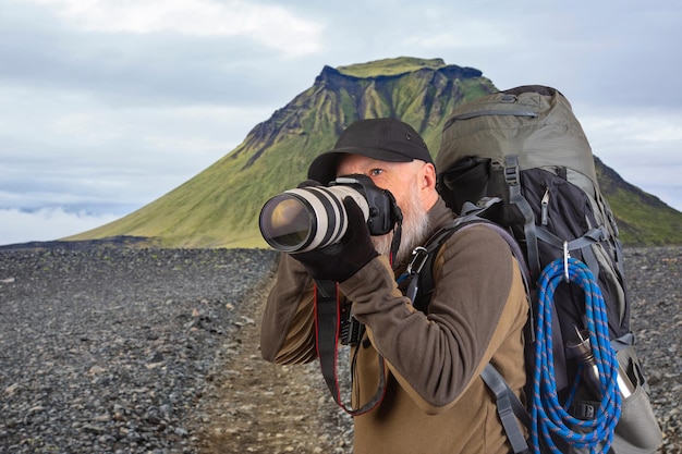 Фото Бородатый мужчина туристический фотограф с рюкзаком фотографирует красоту природы