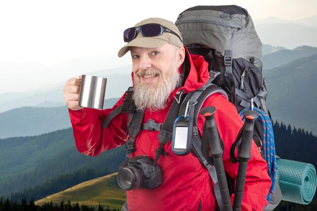 ハイキング機器と山の背景にコーヒーを飲むひげの男の旅行者