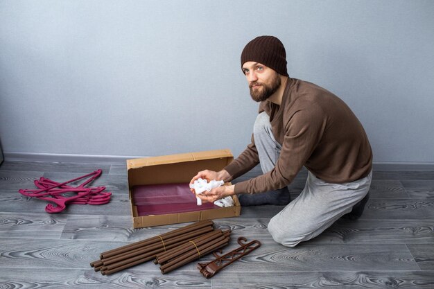 Bearded man unpacks a box of furniture parts and holds plastic connectors in his hands