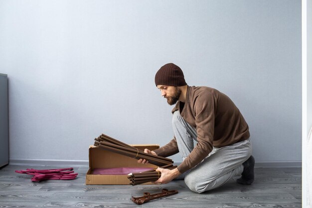 Бородатый мужчина распаковывает коробку с деталями мебели