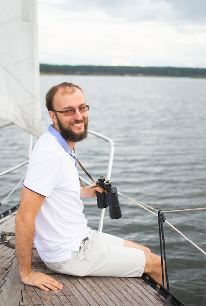 Foto uomo barbuto che guarda binoculare sulla barca a vela