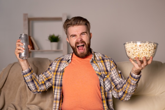 夜に家でポップコーンを食べる映画やスポーツゲームのテレビを見ているひげを生やした男。シネマ、チャンピオンシップ