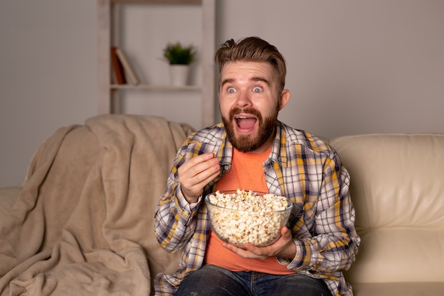 Bearded man watching film or sport games tv eating popcorn in house at night cinema championship and