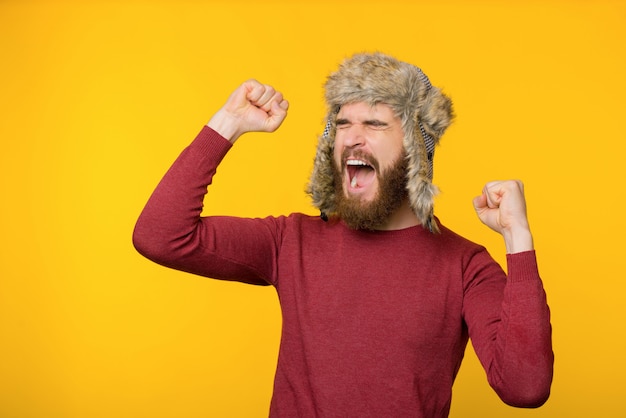 Photo bearded man wearing a comfort winter hat, celebrating, screaming with closed eyes and arms up, isolated background