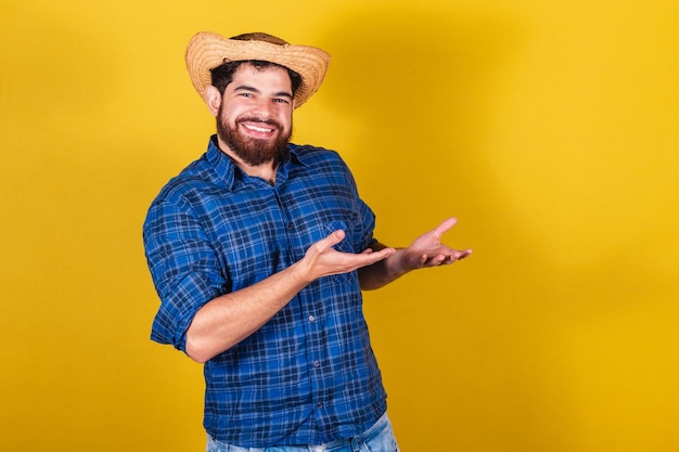 Bearded man wearing typical clothes for the Festa Junina Feast of Arraia de Sao Joao Presenting product presenting something