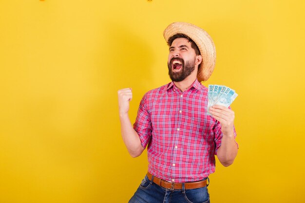 Bearded man wearing typical clothes for party Junina Running and celebrating holding money banknotes victory For the Arraia Party