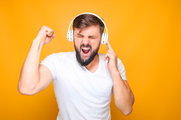 Bearded man in white headphones listening to energetic music and singing emotionally.