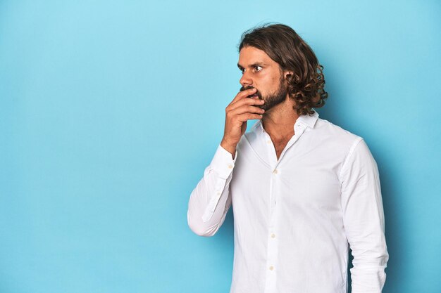 Bearded man in a white shirt blue backdrop thoughtful looking to a copy space