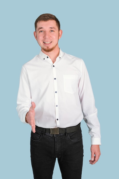 A bearded man in a white shirt makes a handshake gesture while standing on a blue background