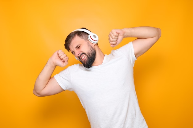 Бородатый мужчина в белой футболке и с наушниками в ушах танцует под музыку.