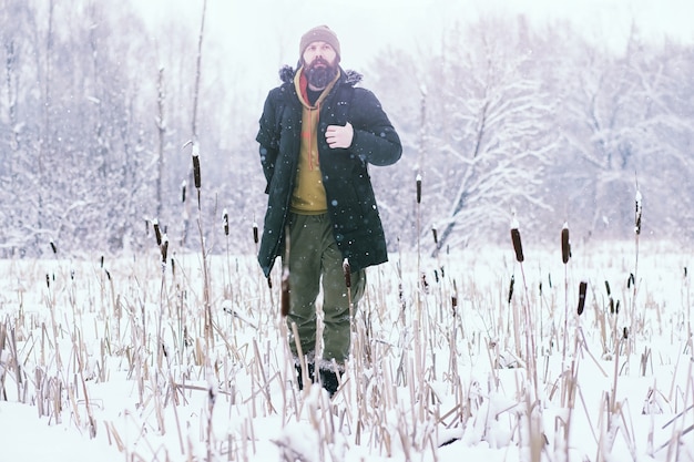 Uomo barbuto nei boschi invernali. attraente giovane felice con la barba a piedi nel parco.