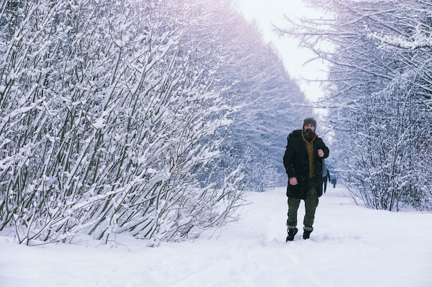 冬の森のひげを生やした男。あごひげを生やした魅力的な幸せな若い男が公園を散歩します。