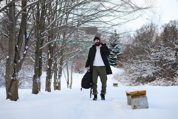 冬の森のひげを生やした男。あごひげを生やした魅力的な幸せな若い男が公園を散歩します。