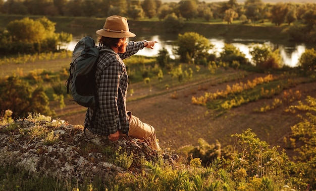 Photo bearded man with backpack pointing at distant river