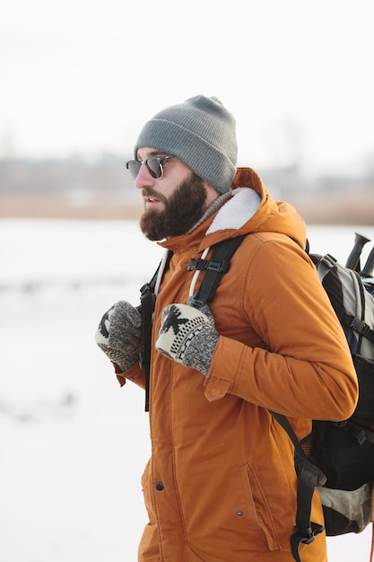 A bearded man with a backpack in warm winter clothes is walking on a frozen lake in winter The concept of hiking and active lifestyle