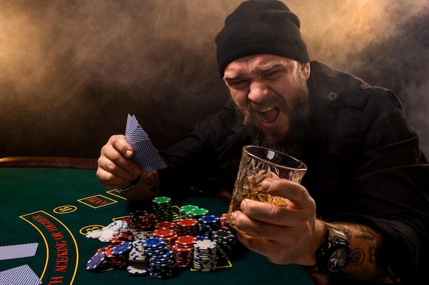 bearded man with cigar and glass sitting at poker table in a casino. gambling, playing cards and roulette.