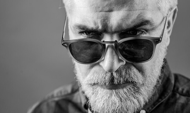 Bearded man with fashion sunglasses Closeup portrait of cheerful young man on gray background with copy space