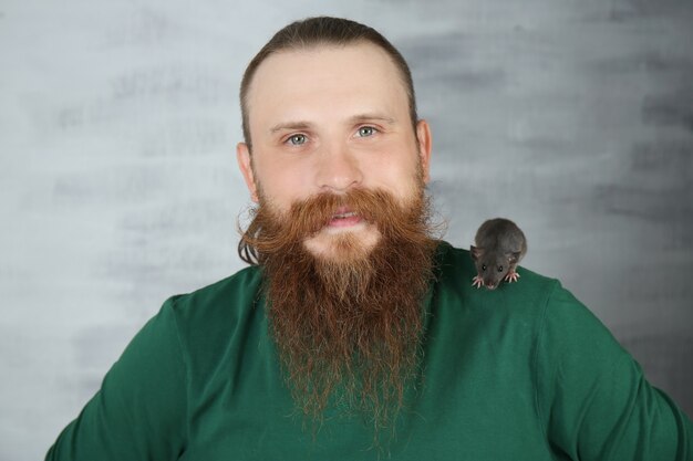 Bearded man with funny rat on color surface