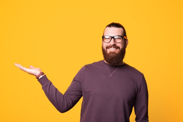 Bearded man with glasses is smiling and is holding his hand up near a free space