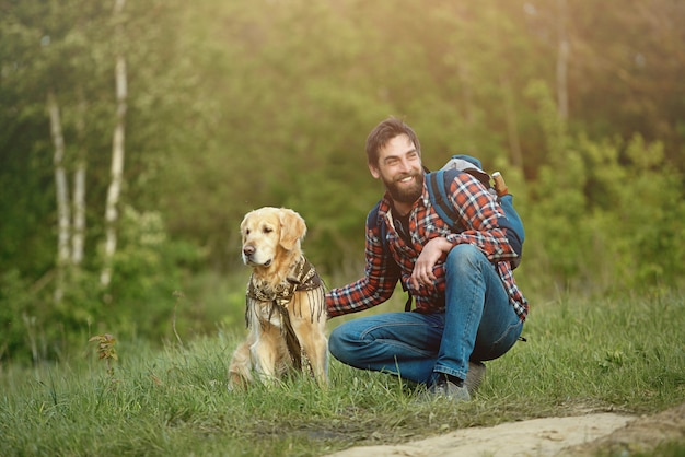 A bearded man with a golden retriever sits against the background of a forest, resting during a trip