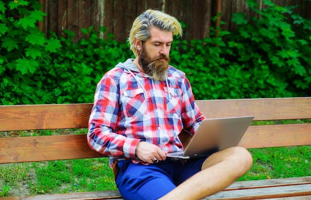 Uomo barbuto con laptop che lavora all'aperto uomo d'affari con taccuino nello studio del parco e lavoro online