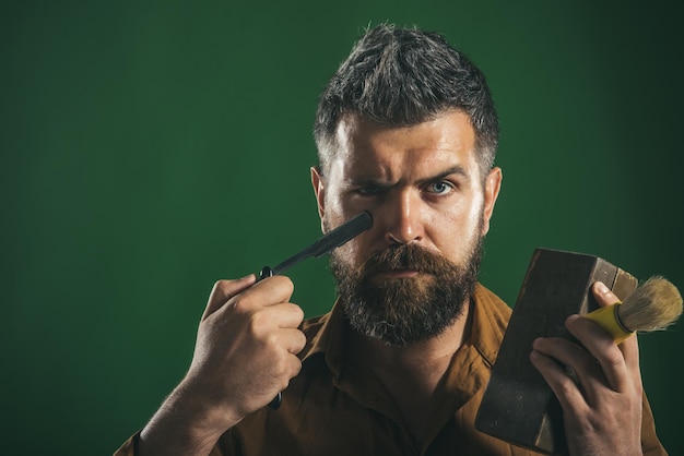 Бородатый мужчина с длинной бородой, жестокий кавказский хипстер с бородой и усами, держит в руках опасную бритву, деревянную шкатулку, щетку для бритья. Реклама парикмахерской. Скопируйте пространство в верхнем углу